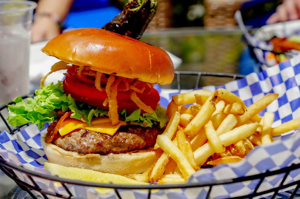 Gourmet burger with crispy fries on blue checkered paper at poolside dining