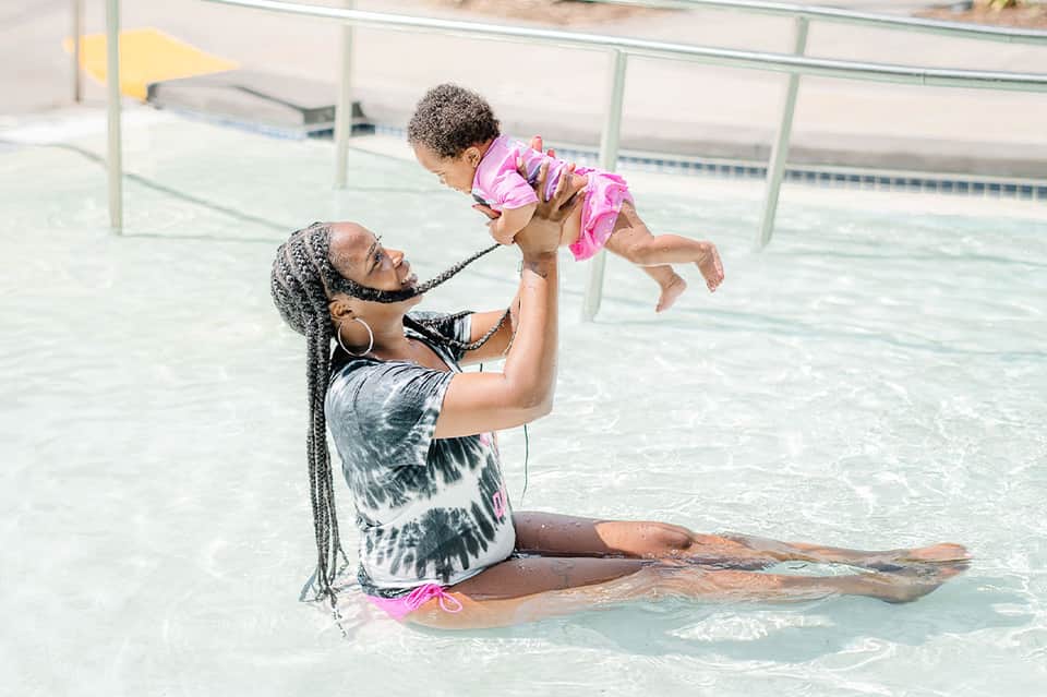 Woman and child playing in shallow pool water at resort