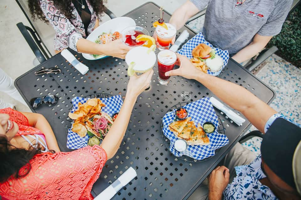 Overhead view of friends dining at outdoor table with tacos, salads, and beverages