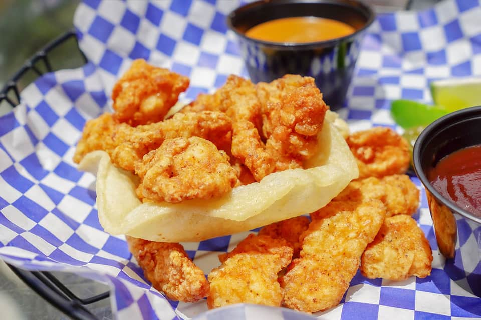 Fried shrimp po'boy sandwich with dipping sauce on blue and white checkered paper