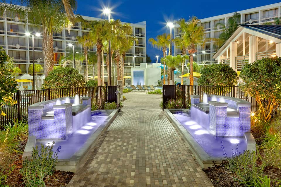 Modern resort courtyard at dusk with illuminated fire pits and palm trees