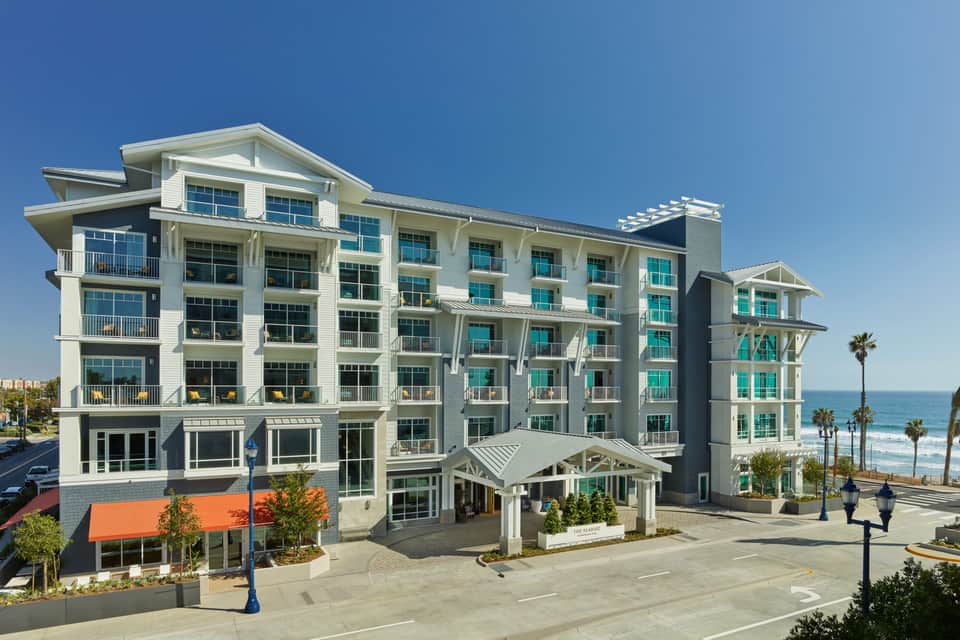 Modern coastal hotel building with white and turquoise exterior, multiple balconies, and beach view