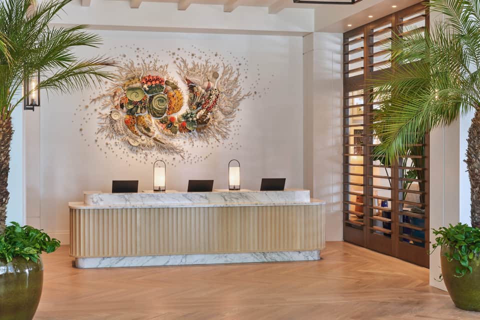 Modern hotel reception desk with marble countertop, wooden slats, decorative wall art, and potted plants