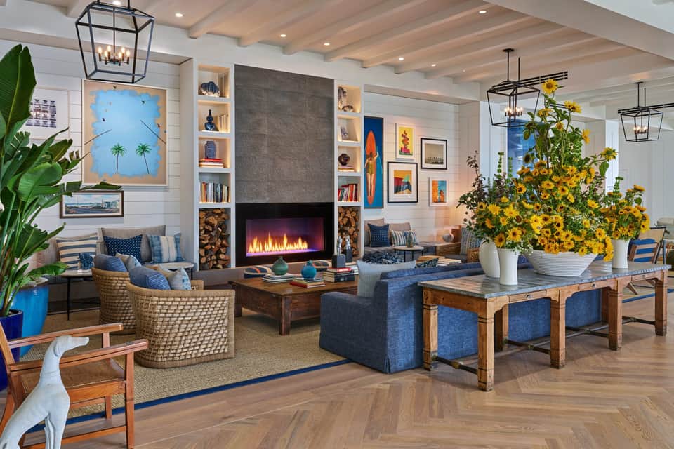 Modern resort lobby with fireplace, blue furniture, yellow flowers, and wooden beam ceiling