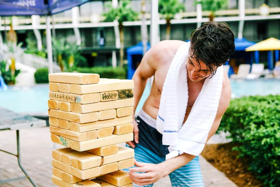 Shirtless man playing giant wooden block stacking game by resort pool area