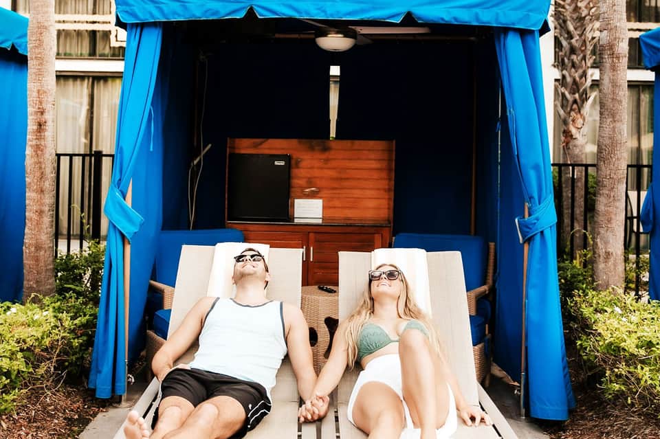 Couple relaxing in blue canopy cabana bed by the pool under clear sky