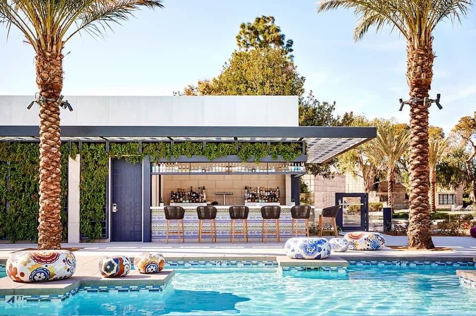 Modern pool bar with white roof, green living wall, and palm trees flanking the structure
