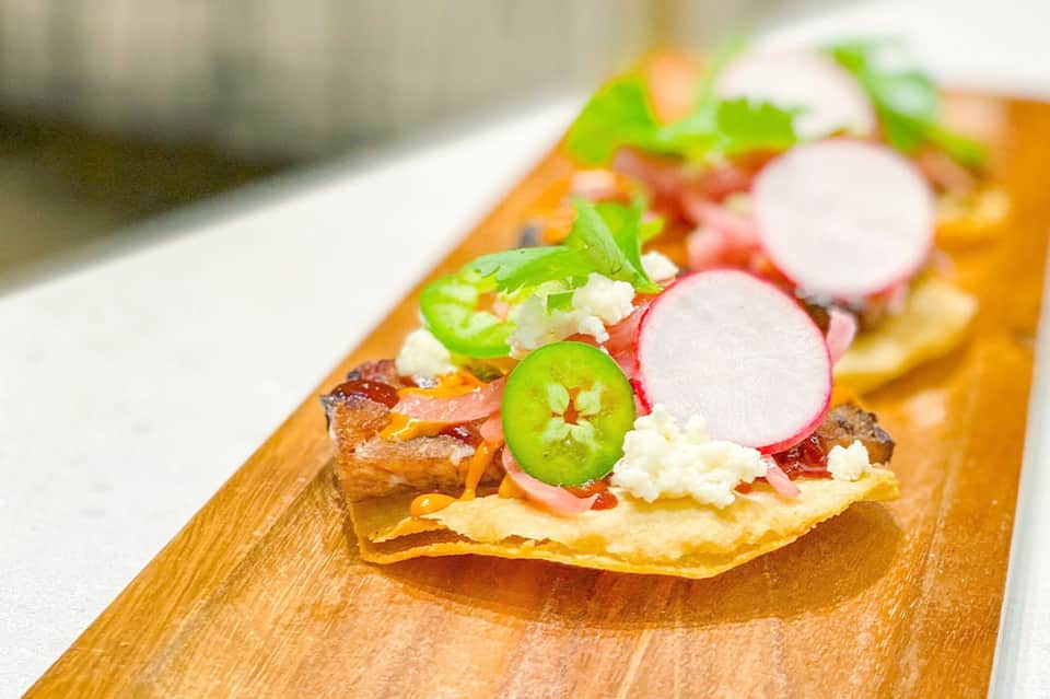 Gourmet tostada appetizer topped with jalapeño slices, radish, queso fresco, and fresh cilantro on wooden board