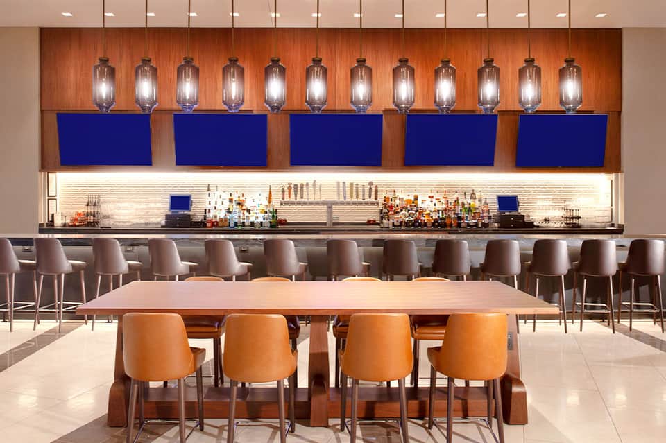 Modern hotel bar with orange chairs, wooden accent wall, and blue-lit shelving with bottles