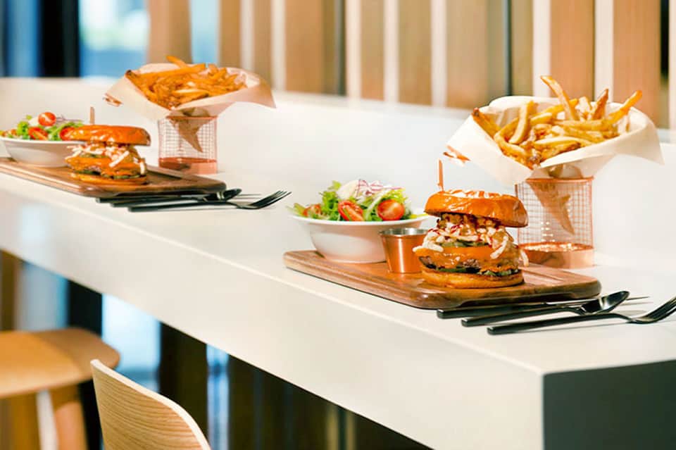 Burgers and fries served on wooden boards with fresh salad on white table setting