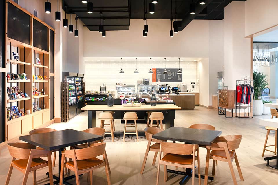 Modern resort café interior with wooden furnishings, shelving, pendant lighting, and service counter