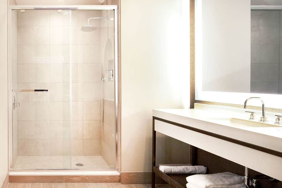Modern bathroom with glass-enclosed shower, white vanity, mirror, and rolled towels