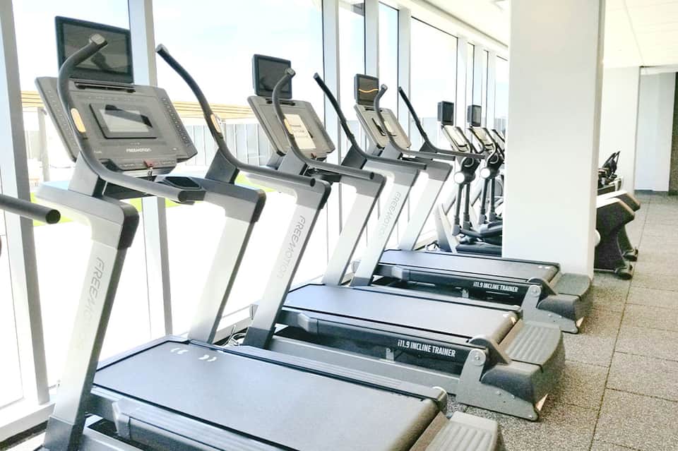 Modern fitness center with rows of incline trainers and cardio equipment by bright windows