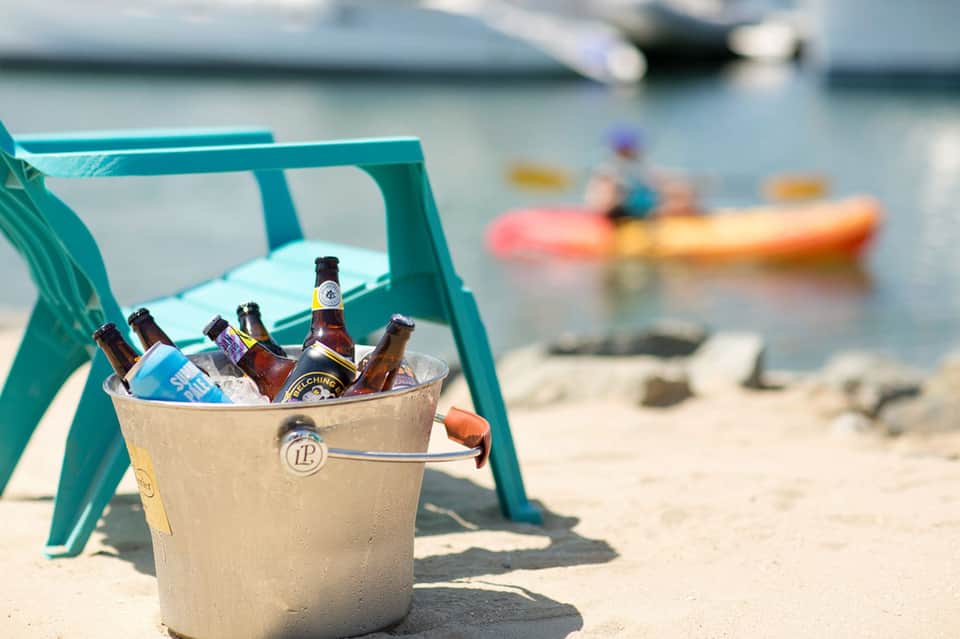 Bucket of cold beers on beach chair with kayakers and boats blurred in background