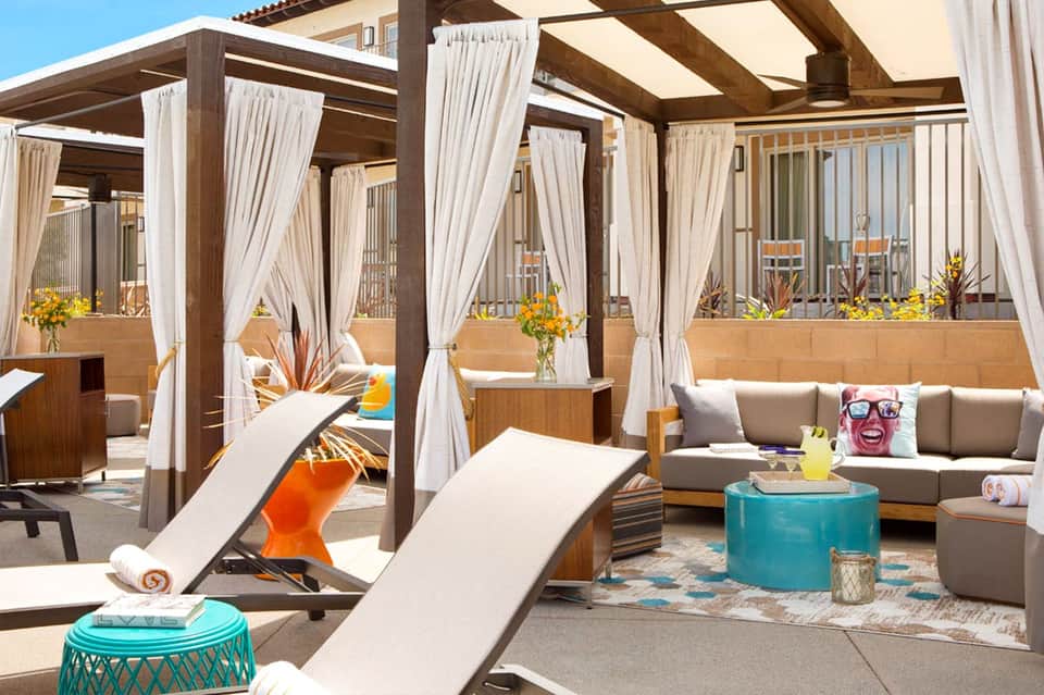 Upscale rooftop lounge with pergolas, white curtains, gray seating, and ocean horizon views
