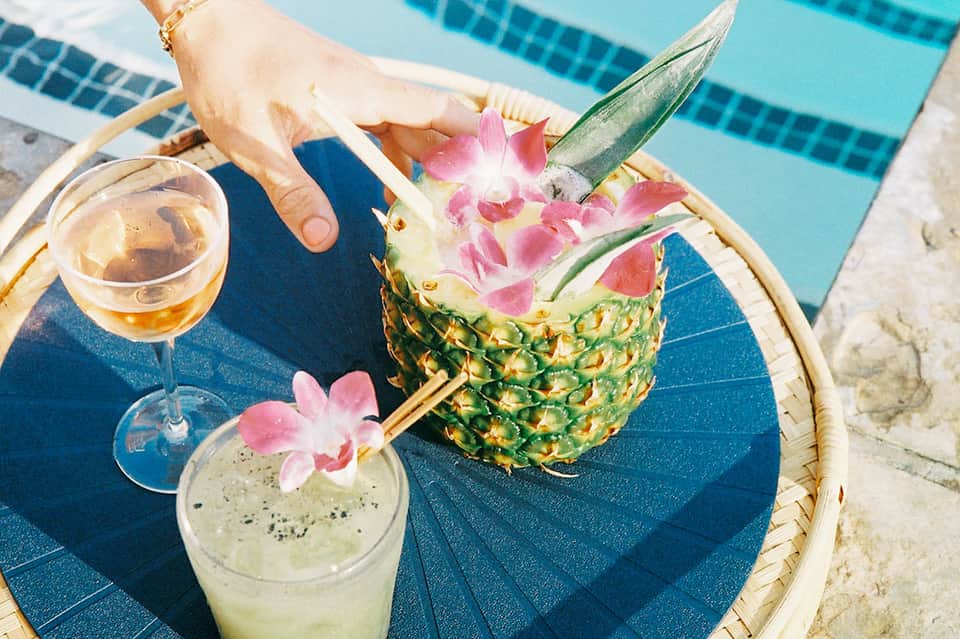 Tropical drinks by the pool including pineapple cocktail and lime beverage with pink flowers