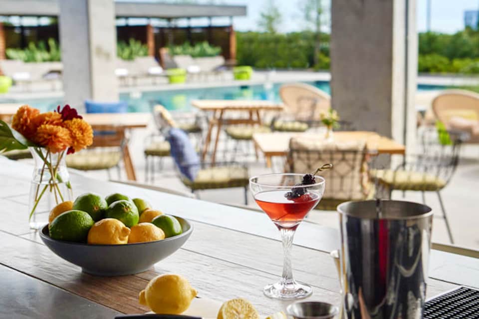 Outdoor poolside bar setup with citrus fruits, cocktail, and lounge chairs overlooking modern resort grounds