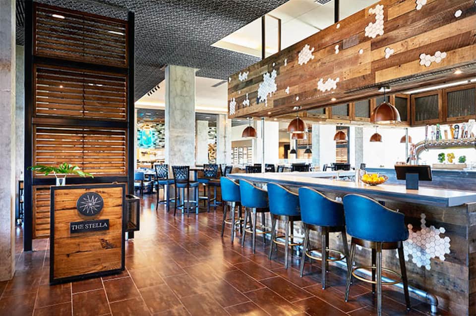Modern bar and lounge with blue stools, wooden wall accents, and pendant lighting