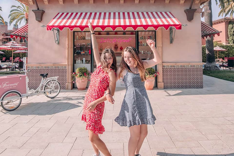 Two women posing outside a pink storefront with red and white striped awning in a resort courtyard