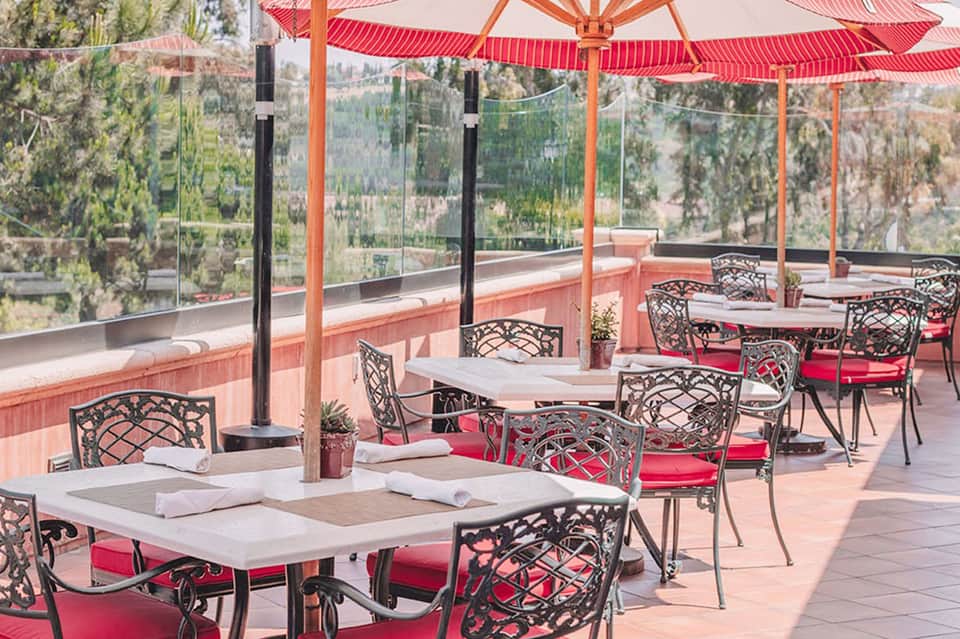 Red umbrellas and decorative seating on a hilltop terrace with panoramic valley views