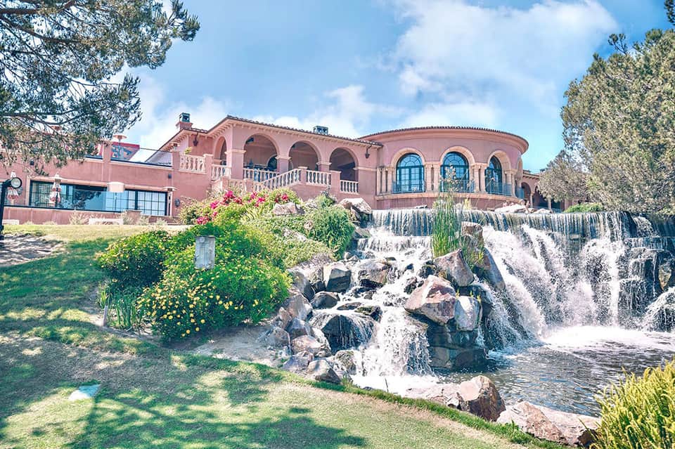Pink villa with arched windows overlooking a cascading waterfall and manicured gardens