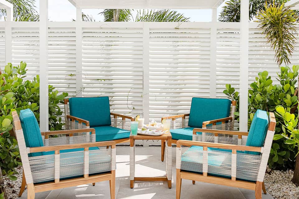 Two teal cushioned wooden chairs facing each other in a private patio enclosed by white horizontal louvers