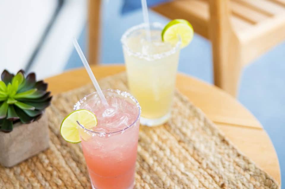Tropical cocktails with lime garnish on wooden table by beach