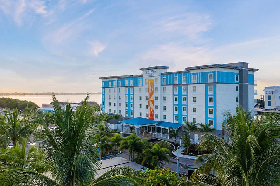 Blue and white Compass hotel building overlooking waterfront with palm trees and landscaping