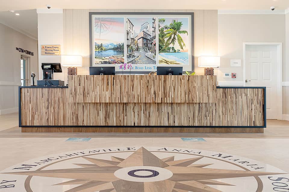 Modern hotel lobby with wooden reception desk, nautical artwork, and compass floor design