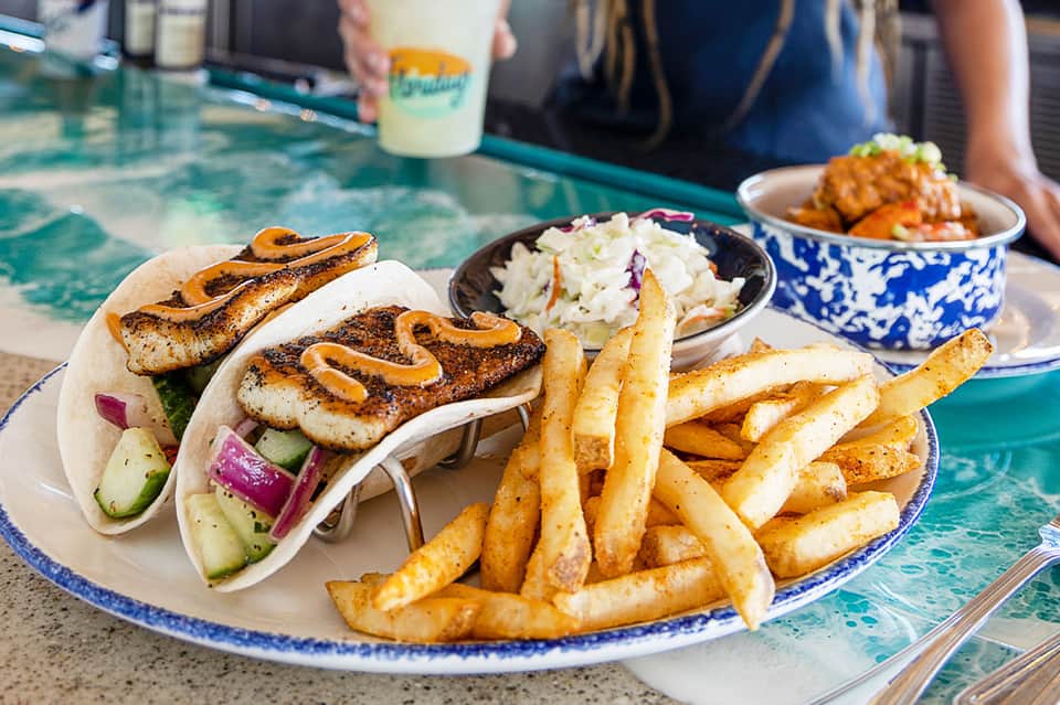 Grilled fish tacos with fries and coleslaw served poolside on decorative blue-white plate