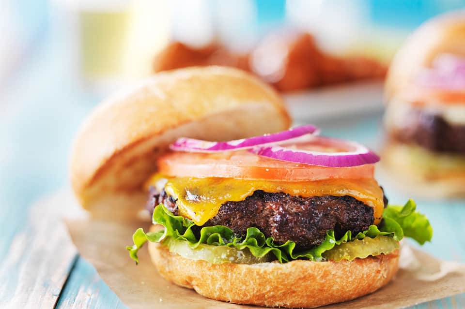 Gourmet burger with melted cheese, lettuce, and purple onion slices on a toasted bun