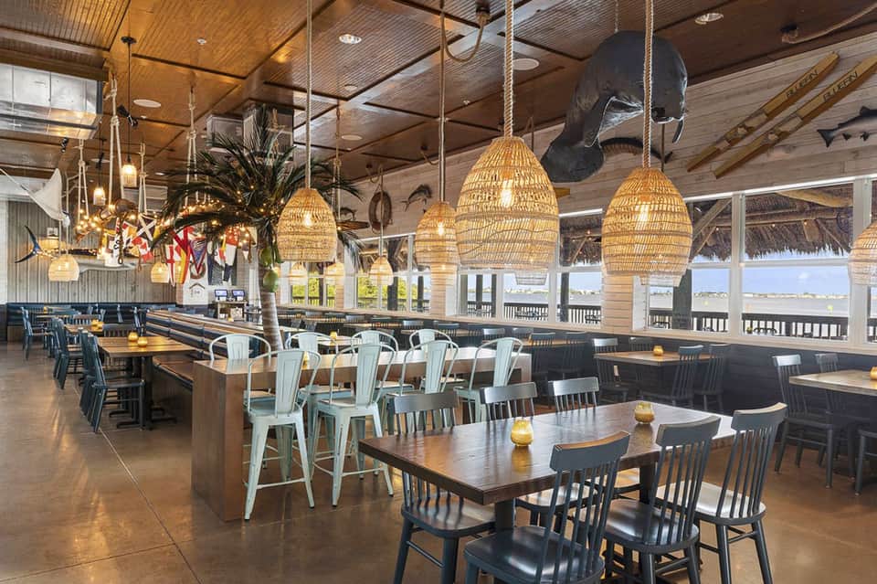 Modern resort dining hall with woven pendant lights, wooden ceiling, ocean views, and mixed seating at tables and bar