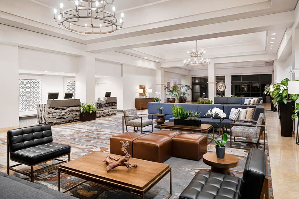 Luxury hotel lobby with modern furnishings, decorative plants, leather seating, and contemporary chandeliers