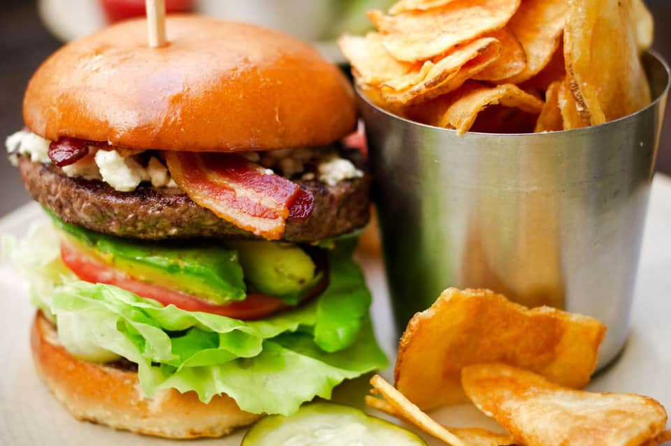 Gourmet burger with bacon and lettuce beside golden potato chips in metal container