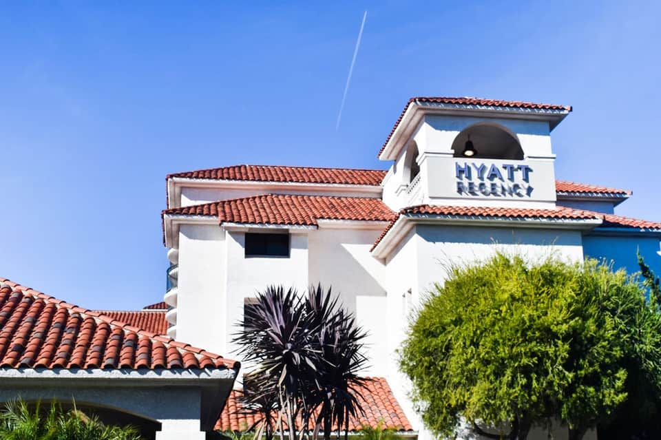 Hyatt Regency hotel exterior with white walls, red tile roofs, and tropical landscaping under blue sky