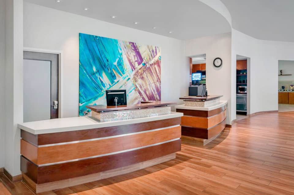 Modern hotel reception desk with wood and marble finishes, colorful abstract artwork, and contemporary design