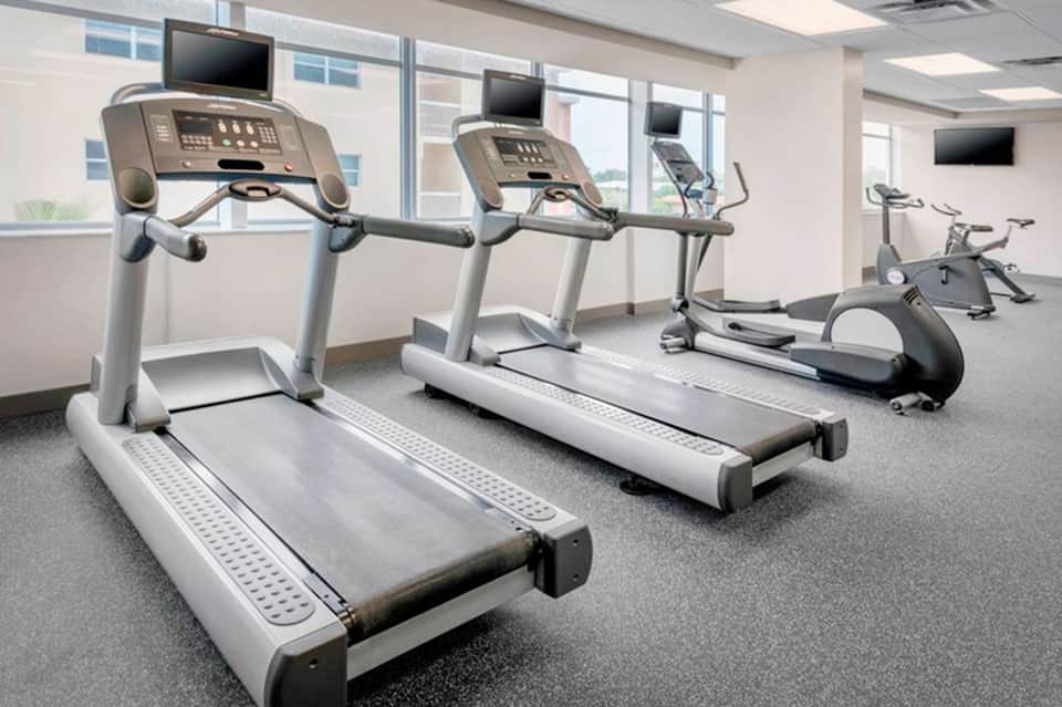 Bright fitness center with multiple treadmills facing large windows overlooking the landscape