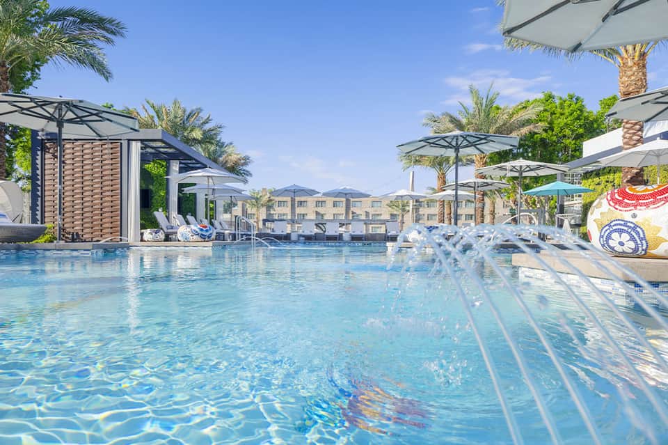 Resort swimming pool with loungers, umbrellas, and palm trees under blue sky