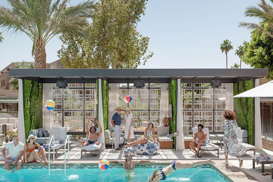 Poolside cabanas with guests enjoying amenities under black pergolas with ivy accent walls