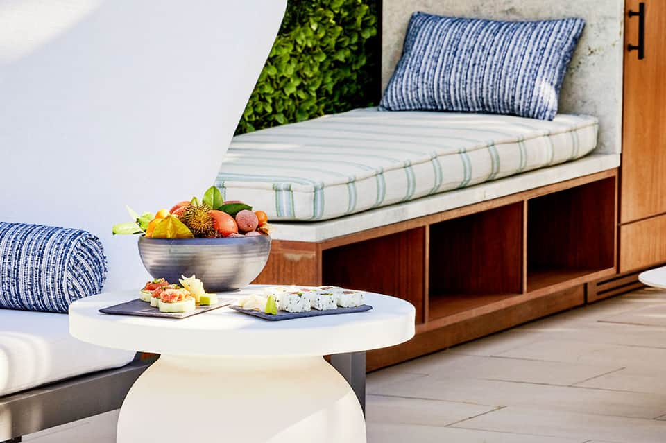 Outdoor bench seating with striped cushion, side table with fresh fruit bowl and appetizers