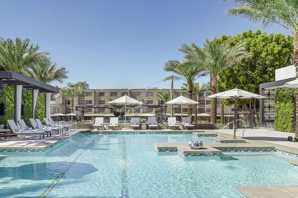 Luxury resort pool with loungers, umbrellas, and palm trees under clear blue sky