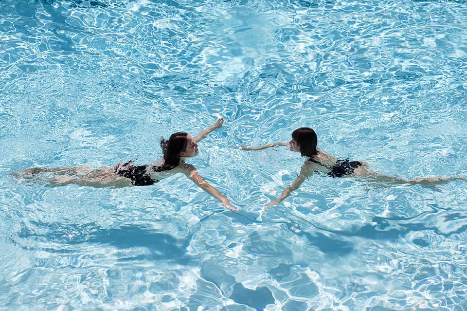 Two women swimming together in crystal clear turquoise pool water