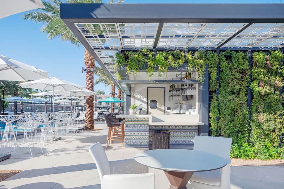 Modern outdoor bar with living green walls, white furniture, and covered pergola seating area