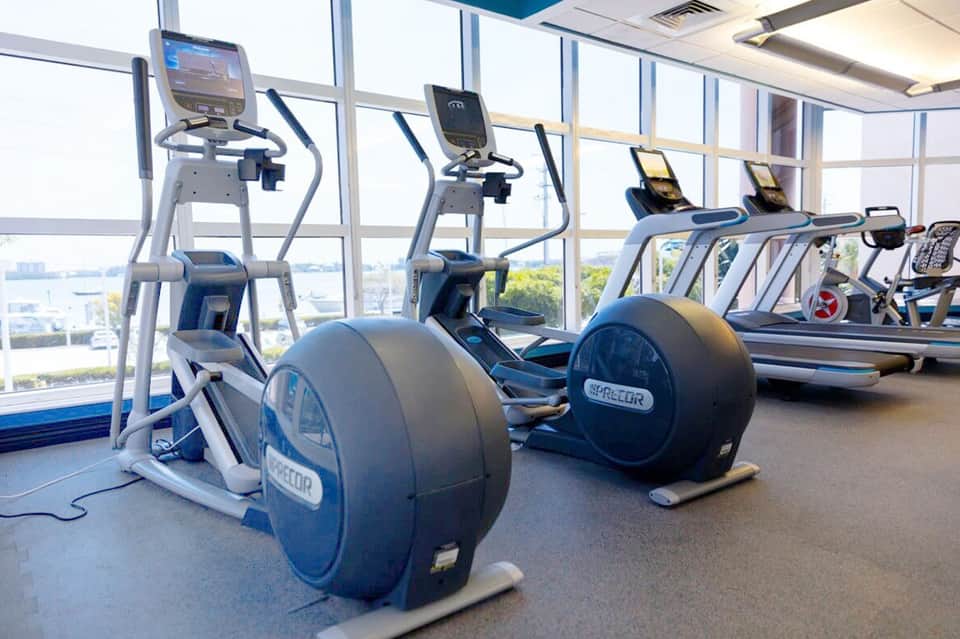 Fitness center with elliptical machines and treadmills lined along windows overlooking cityscape and green landscape