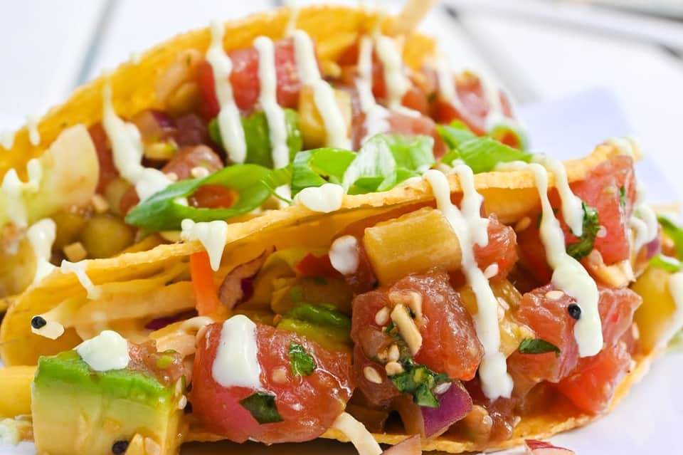 Gourmet fish tacos topped with white sauce, fresh toppings, and vibrant garnishes