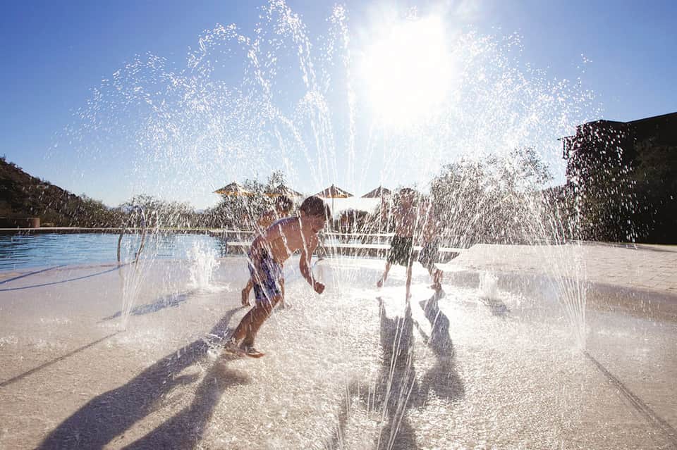 Child running through water splash pad at outdoor pool area with clear sky