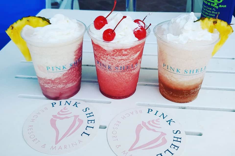 Three colorful layered cocktails with pineapple garnish at Pink Shell resort bar