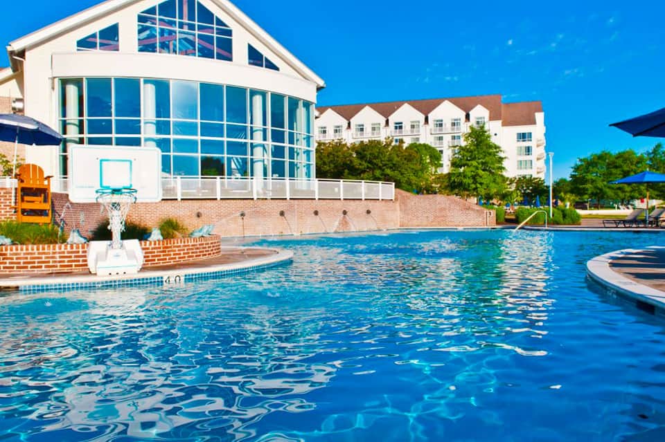 Large outdoor swimming pool with modern white pavilion and residential buildings under clear blue sky