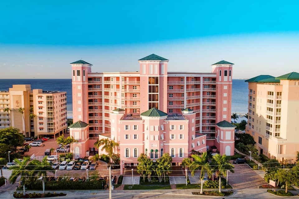 Pink beachfront resort with turquoise-roofed towers overlooking the ocean and palm trees