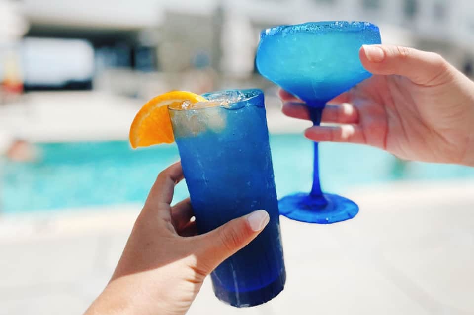 Vibrant blue cocktails by the pool with orange garnish and colorful frozen glasses